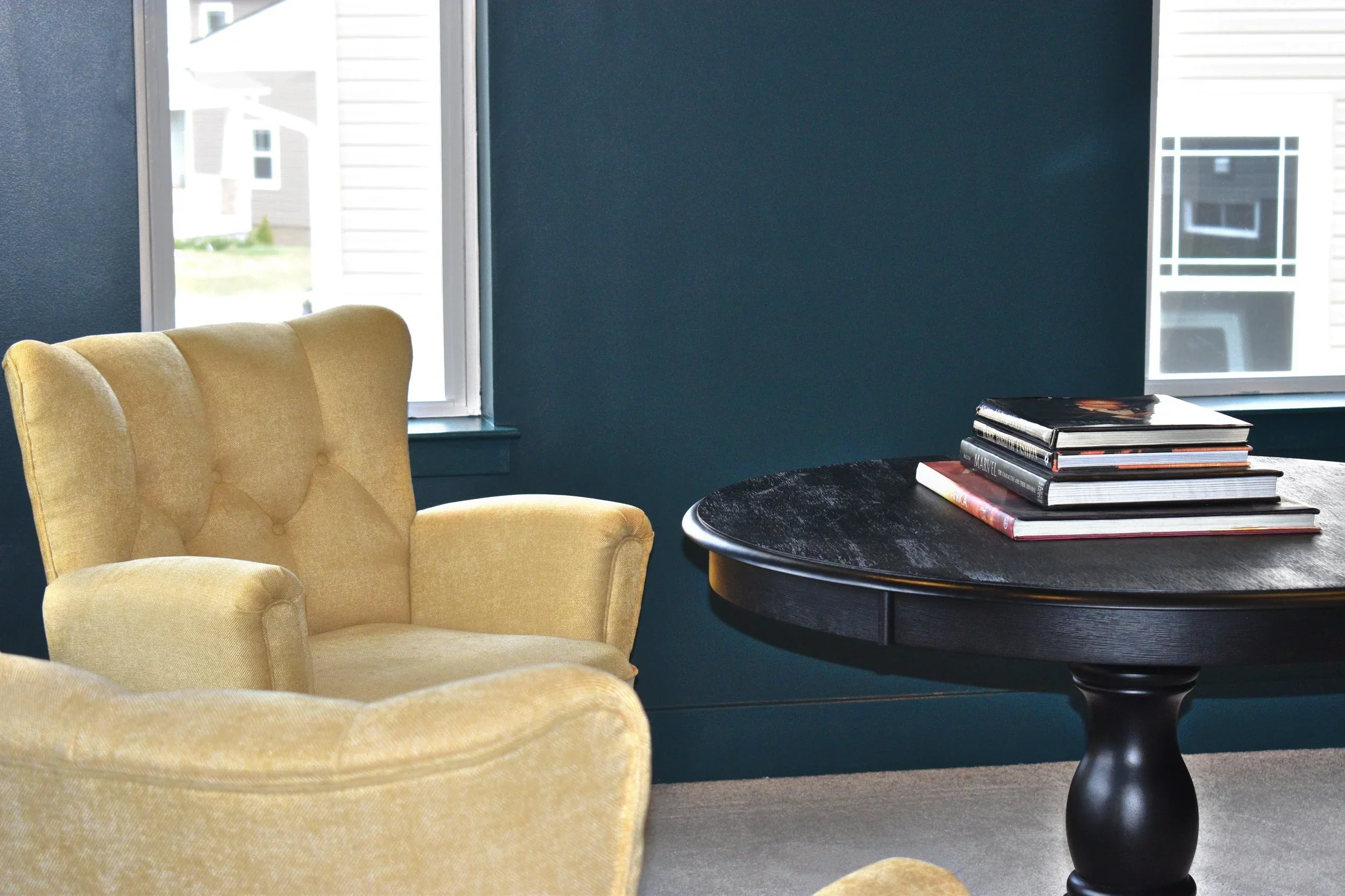 Deep teal accent wall in modern living room with yellow chair and black side table