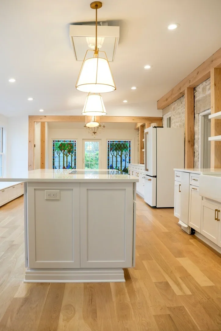 Modern kitchen with white cabinetry, quartz island, hardwood floors, and brass pendant lights