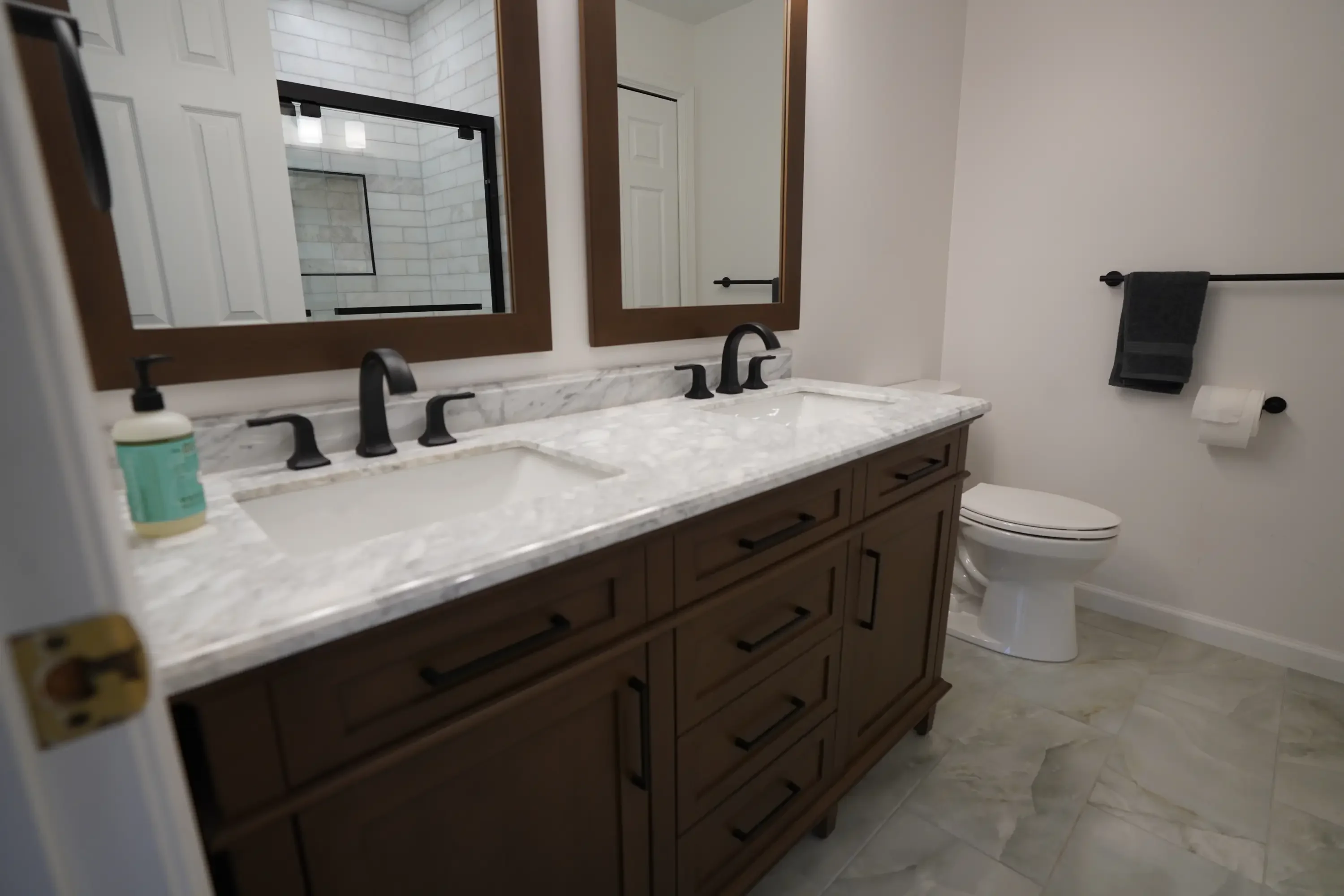 Modern bathroom with dark wood double vanity, marble countertop, and black fixtures