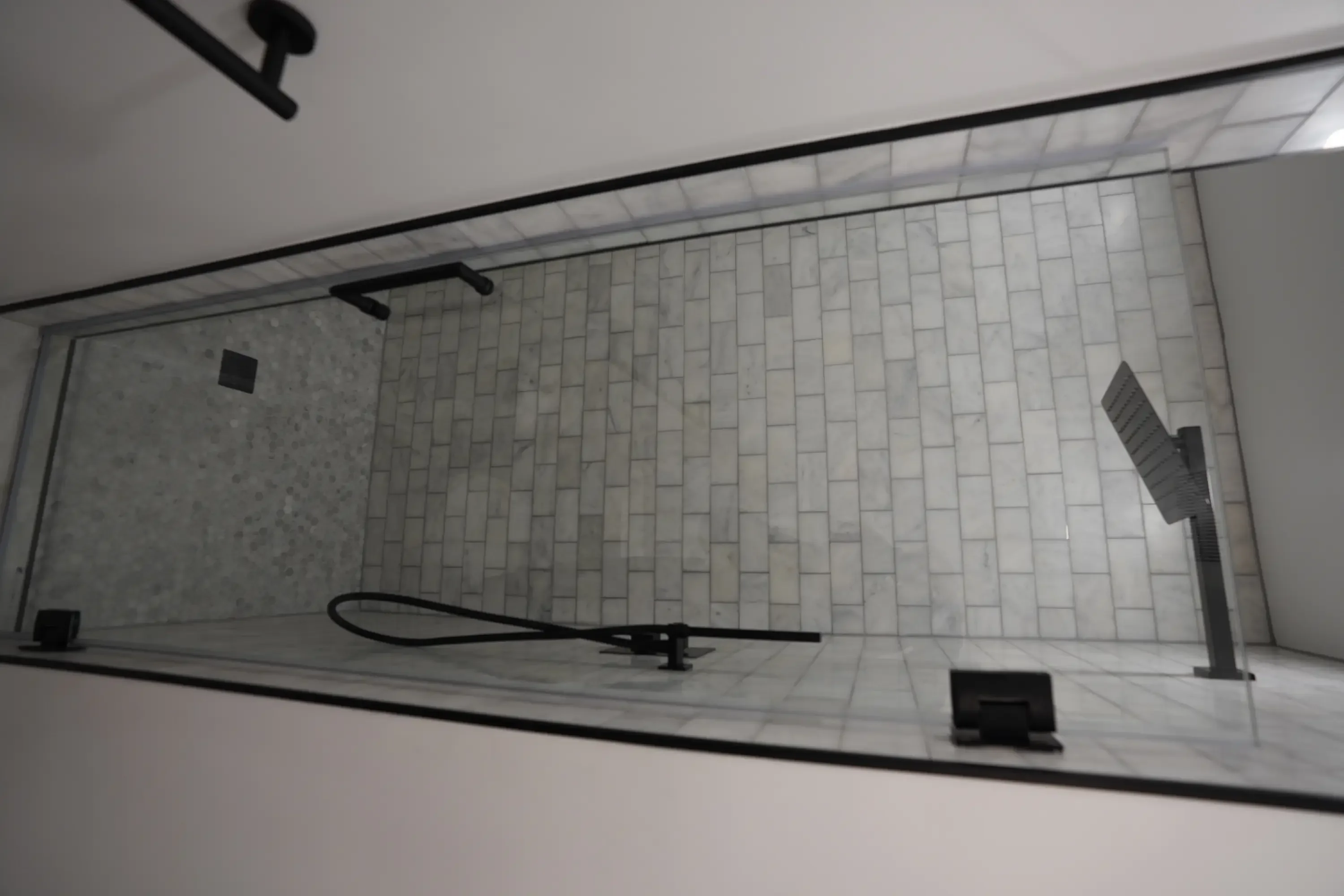 Modern bathroom shower with white subway tile walls, frameless glass door, and black fixtures