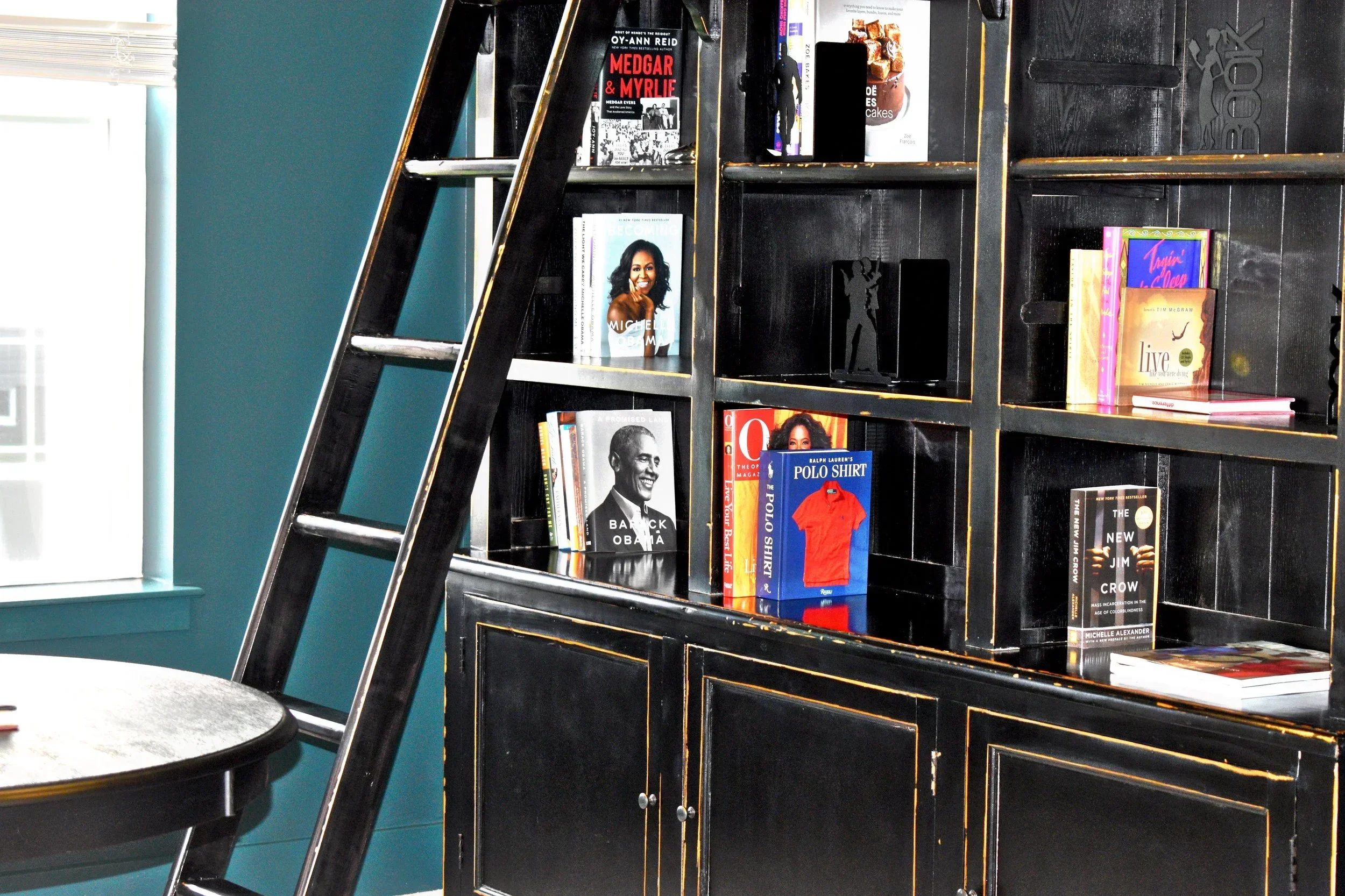 Black built-in shelving with brass trim and lower cabinetry against teal wall with library ladder