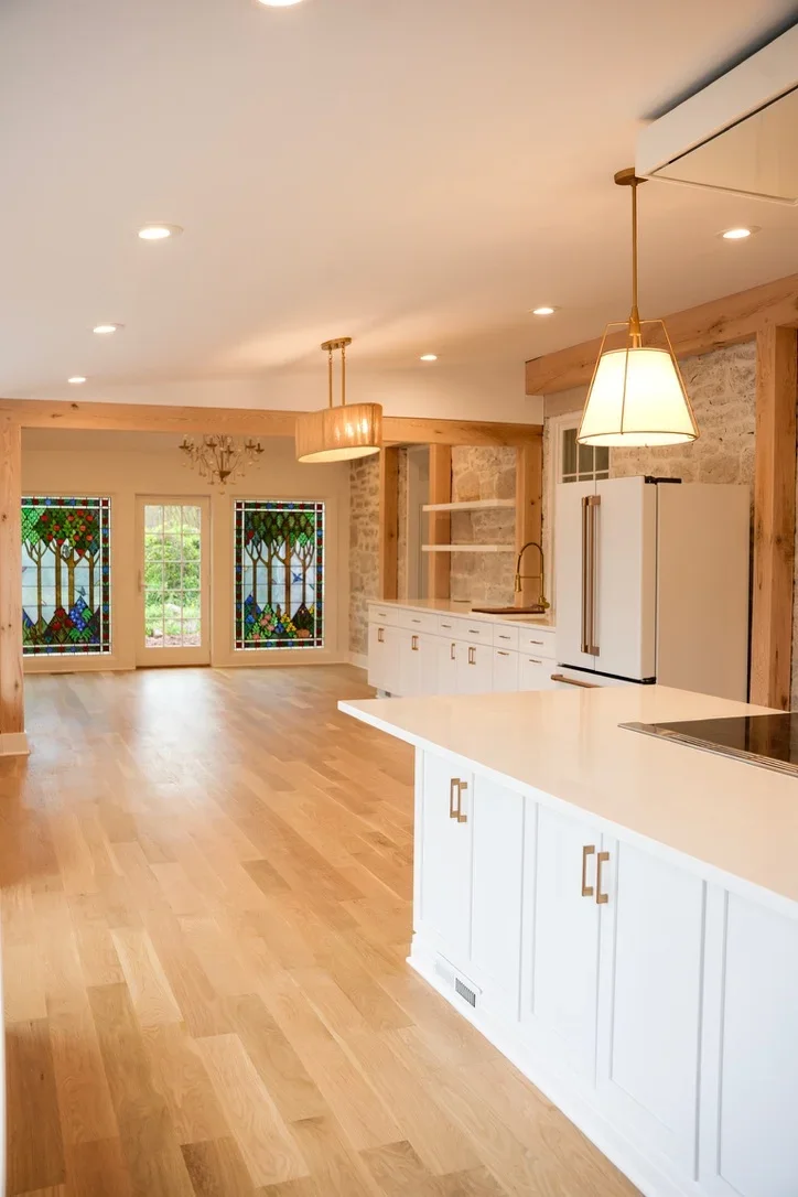 Modern kitchen with white cabinets, quartz counters, and open living area with hardwood floors