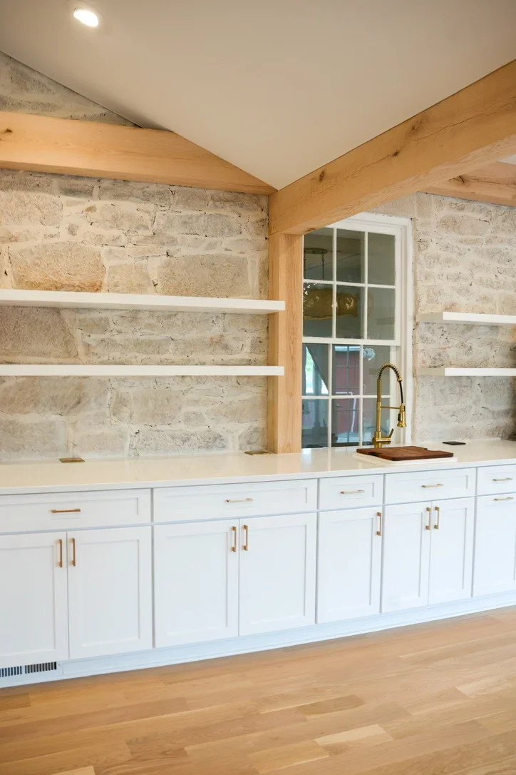Modern kitchen with white cabinets, stone brick backsplash, wood beams, and floating shelves