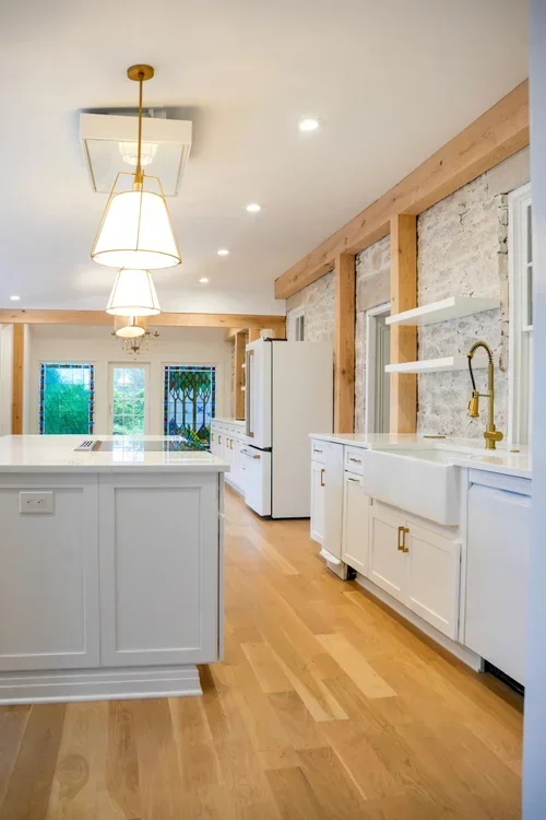 Modern kitchen with white cabinets, exposed wood beams, and stone accent wall