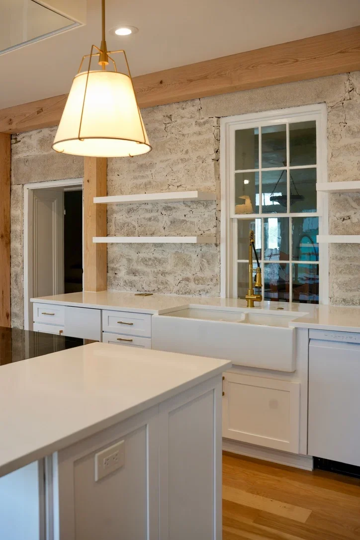 Modern kitchen with white cabinets, stone accent wall, and brass pendant light