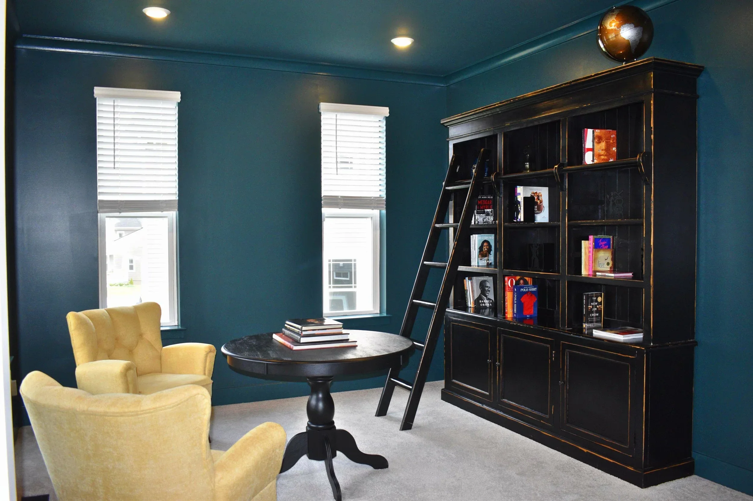 Teal library room with black built-in cabinetry, yellow chairs, and white shutters