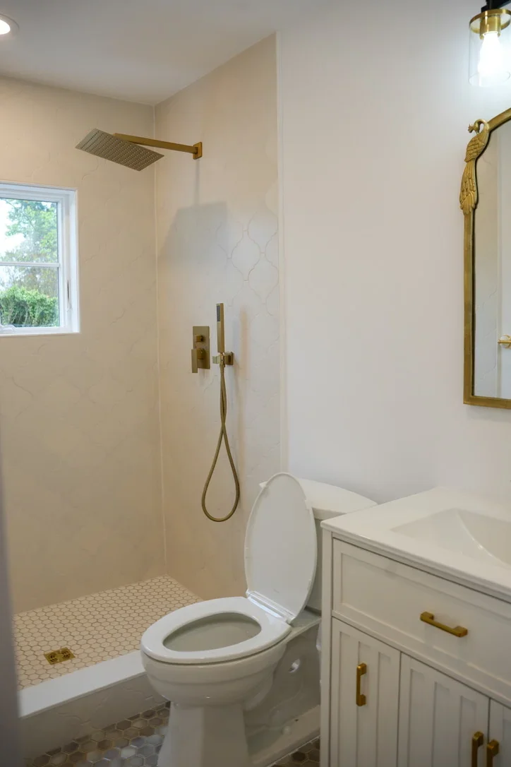 Modern bathroom with walk-in shower, brass fixtures, white vanity, and penny tile flooring