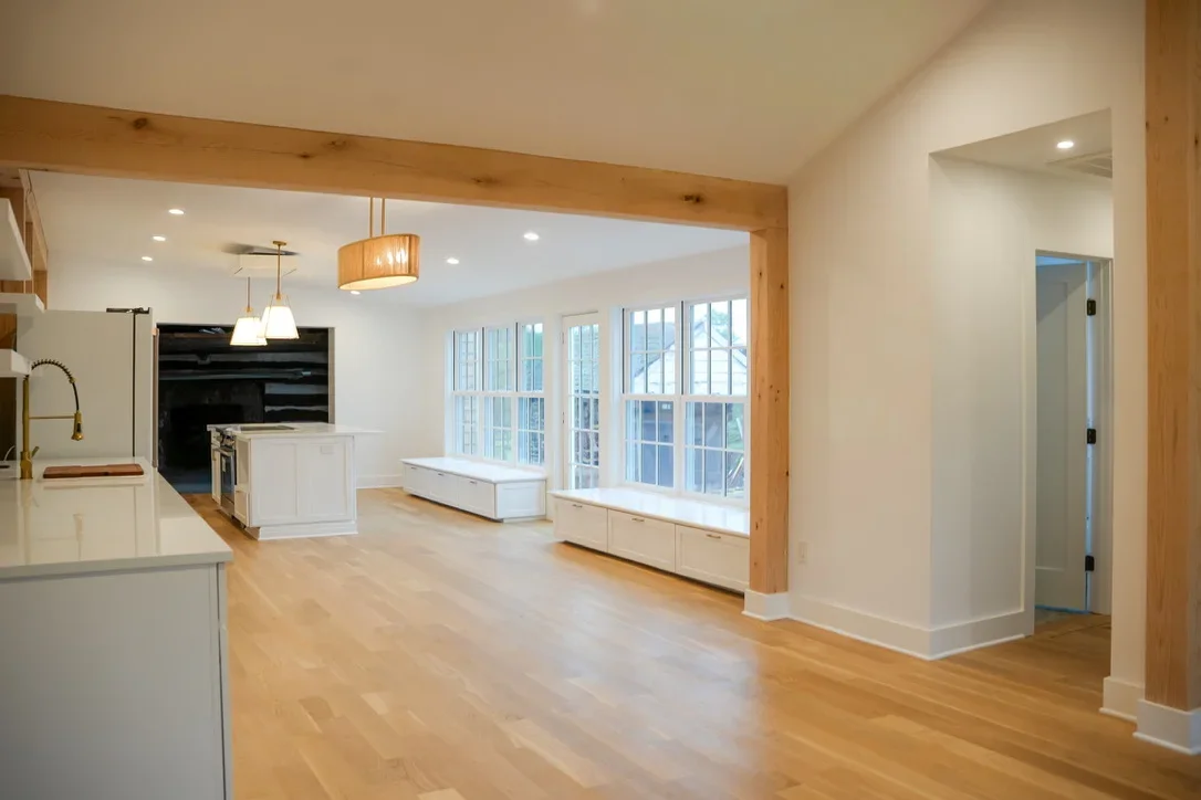 Modern open concept kitchen with white cabinetry, hardwood floors, and timber beam accents