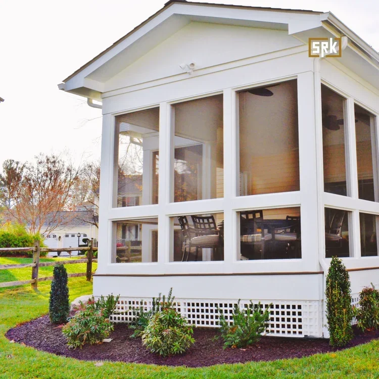 White sunroom addition with large windows, pitched roof, and landscaped foundation