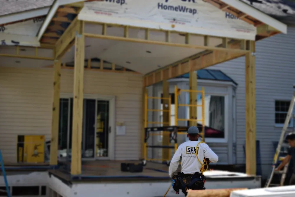 Contractor working on wooden porch framing with yellow posts and roof structure