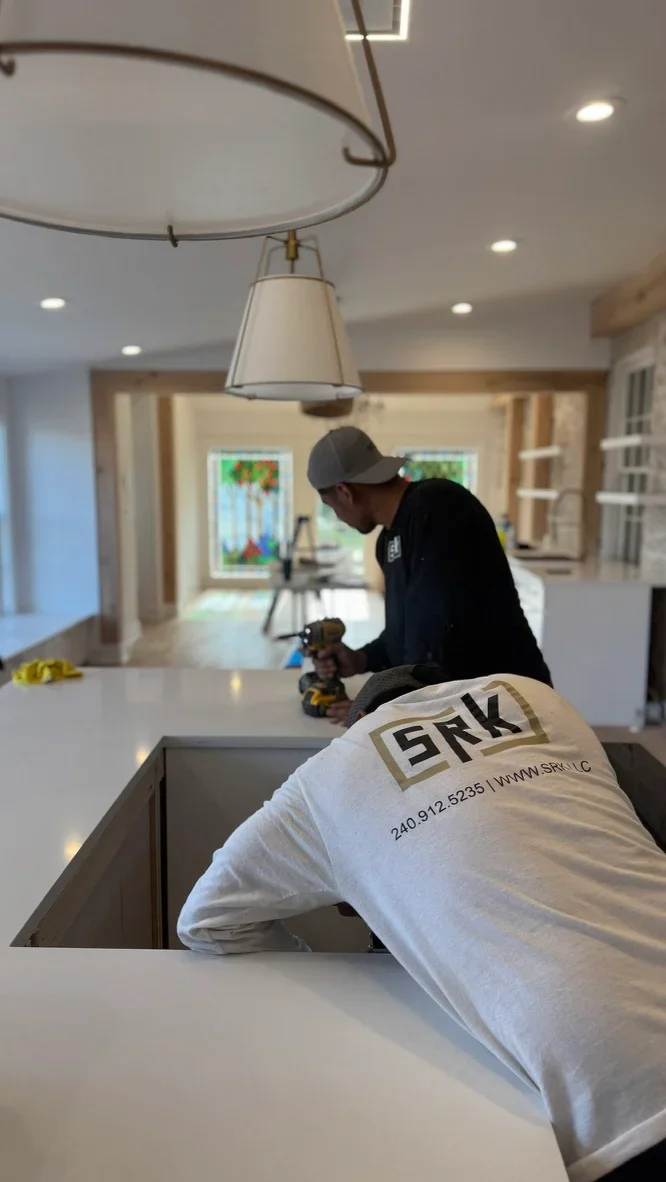 Contractor installing pendant light fixture over newly constructed kitchen island with white countertop