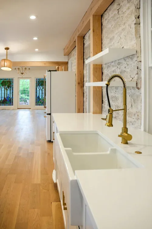 Modern kitchen with white cabinetry, dual brass faucets, and exposed wood beams